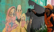 A municipal employee in Jakarta, Indonesia, paints over a Covid-19 awareness campaign. (© picture alliance / NurPhoto / Agoes Rudianto)